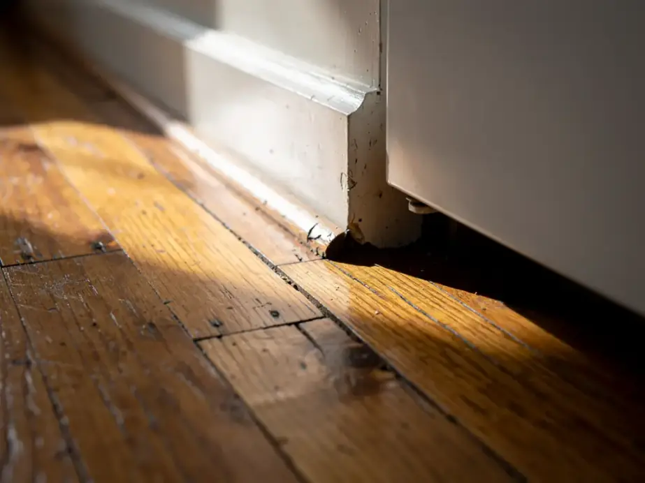 Baseboard gap beside a refrigerator toe-kick on oak floorboards